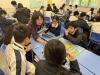 The instructor teaches students how to play a board game about financial management. 